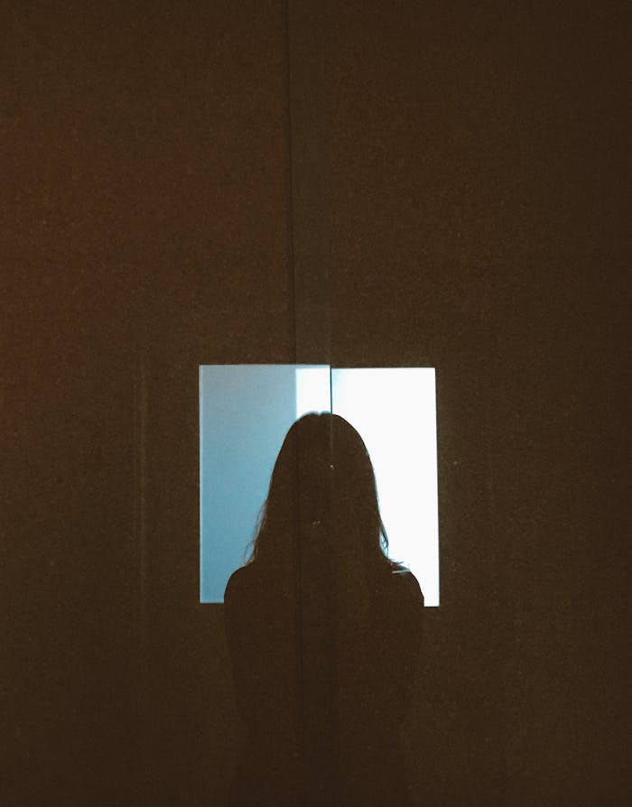 Silhouette of a woman standing before a window projecting light indoors.