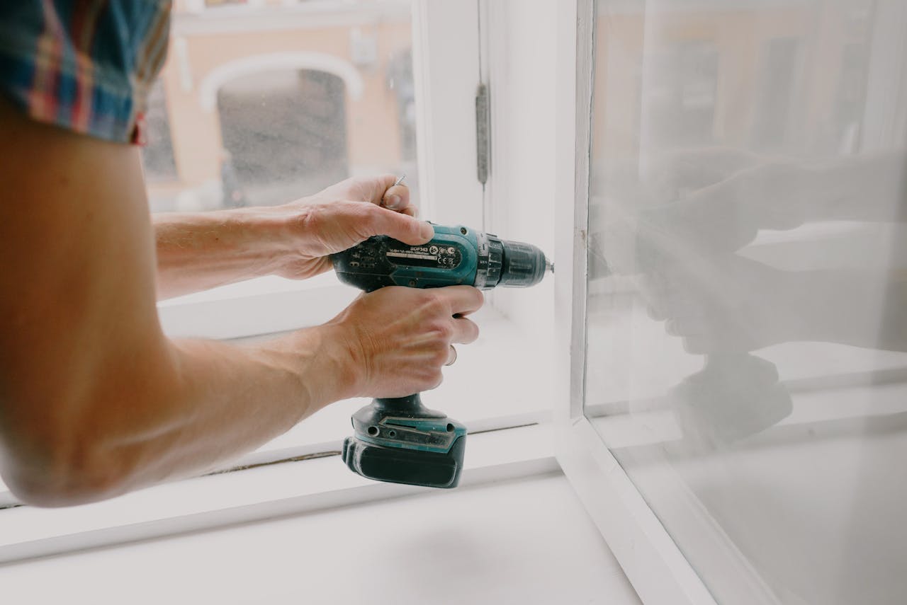 home-img A person using an electric drill to repair or install a window indoors.