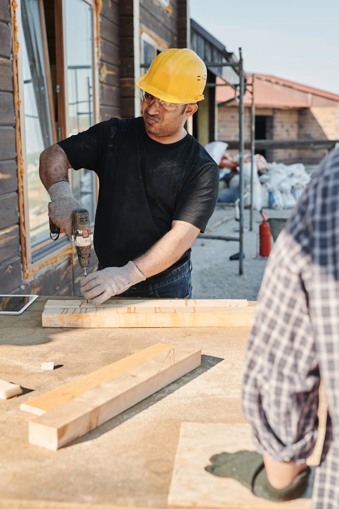 gallery-05 A construction worker using a drill on wood at a building site outdoors.